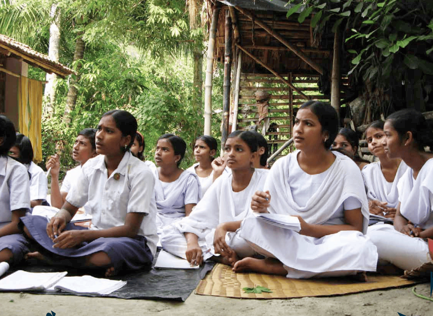 A group of people sitting on mats outside writing in notebooks 